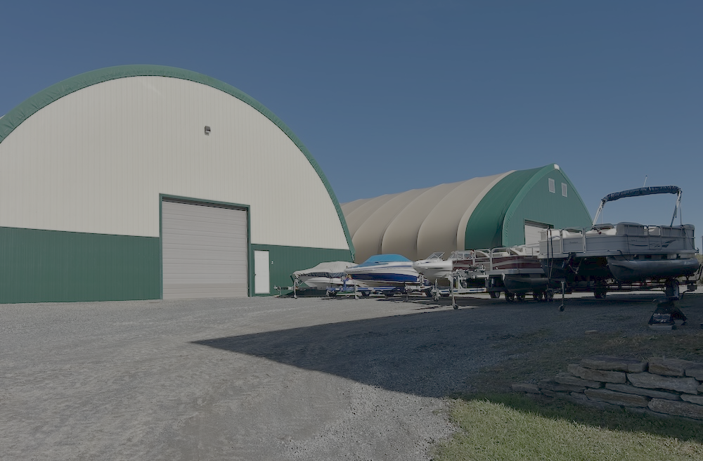 Boat, hot rod, and Class C motorhome in front of a Quonset barn
